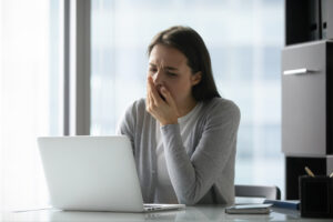 woman in front of open laptop at office desk and yawning